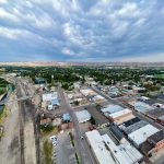 Emmett ID 19 Aerial view of Emmett ID, a small town with grid-like streets, industrial buildings, a canal, and railroad tracks, surrounded by green trees and open countryside under a cloudy sky.