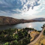 Emmett ID 7 A winding river bordered by hills and a tree-lined area with buildings, adjacent to a road curving along the water under a partly cloudy sky at sunset. In Emmett, ID.